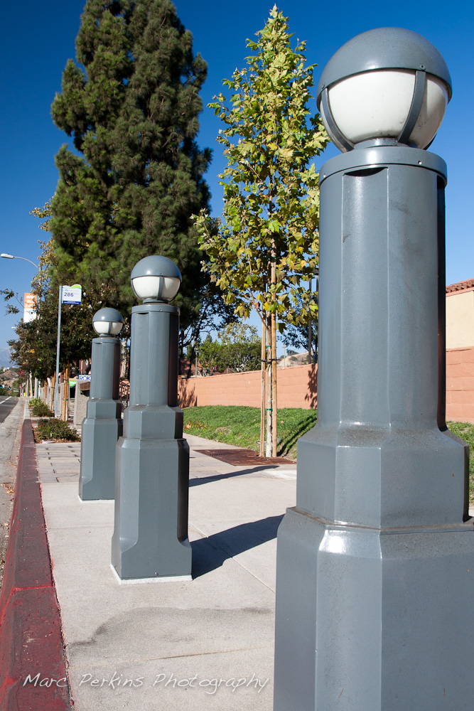 Three blue-gray metal lights (that remind me of little soldiers in a row) stand at the bus stop on the northeastern corner of Gand and Diamond Bar. Plenty of blue sky is visible in this wide angle shot. This was part of the 2015 rebuild of the Grand Avenue and Diamond Bar Boulevard intersection for Diamond Bar's 2015 "Grand Avenue Beautification" project, landscape architecture for the project was by David Volz Design.