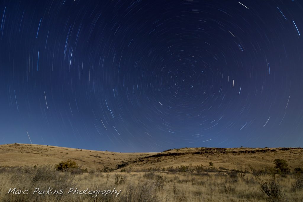 A long-exposure night image with moonlit illuminated hills and stars rotating around Polaris.